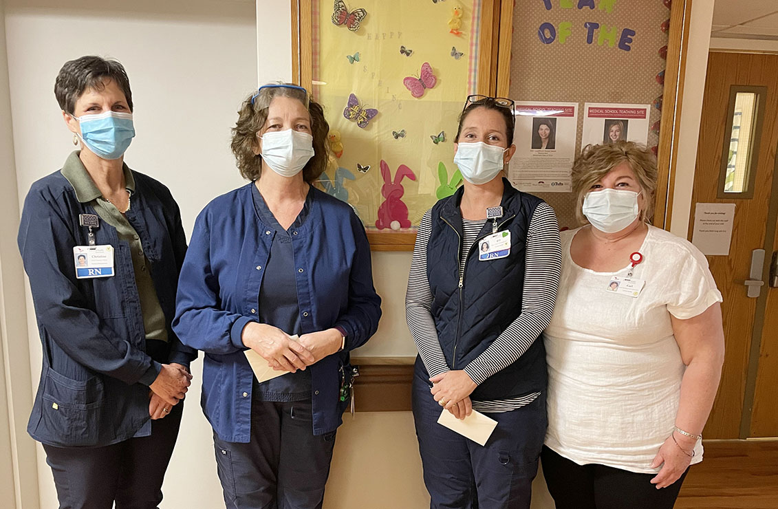 four women wearing masks standing together in front of a bulletin board