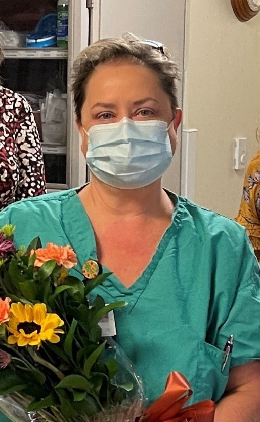 Woman in scrubs and mask holding a bouquet of flowers