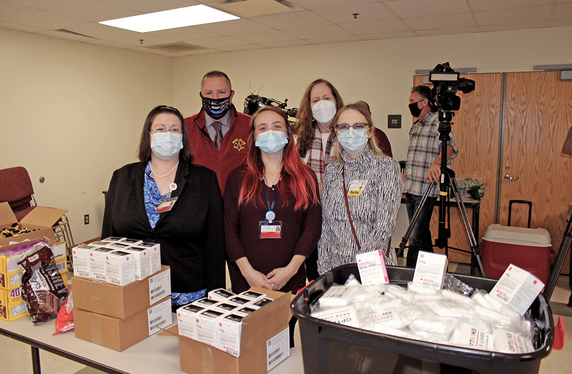 group of men and women wearing masks standing next to a table of supplies for harm reduction bags