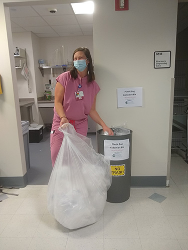 woman in scrubs and masks holds large bag of recycled materials in a hospital hallway